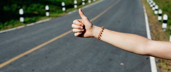 Ausgestreckte Hand mit Daumen hoch an einer Straße